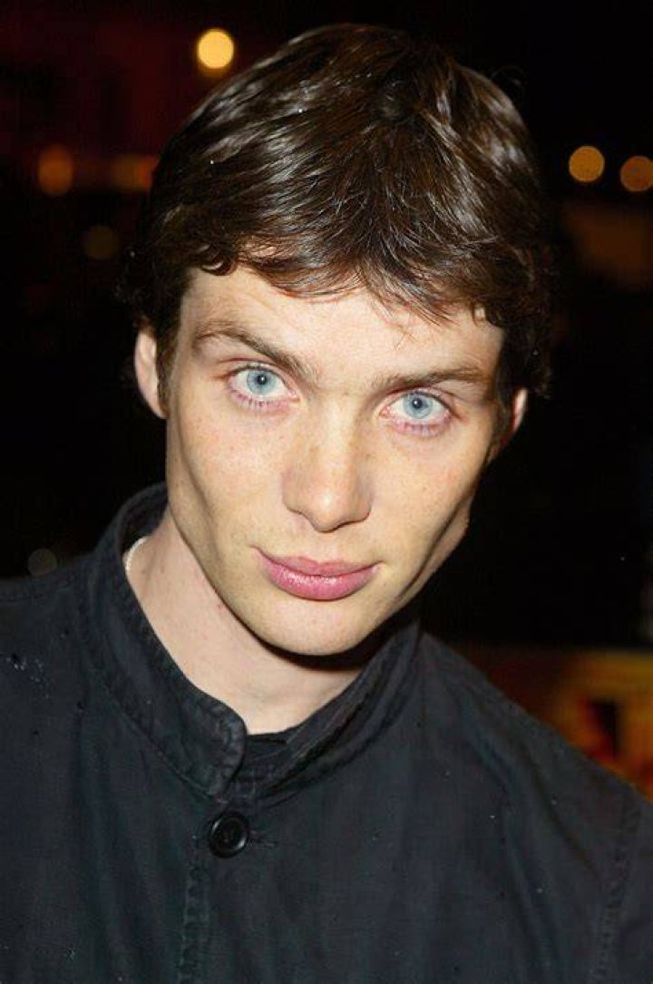 Cillian Murphy talking with wide-eyed intensity to a group of men in Oppenheimer