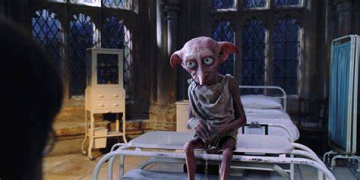 Dobby sits at the end of Harry Potter's bed