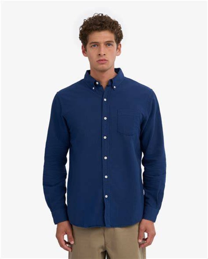 expat in blue shirt and brown hat standing on a brown wooden bridge overlooking a canal in venice