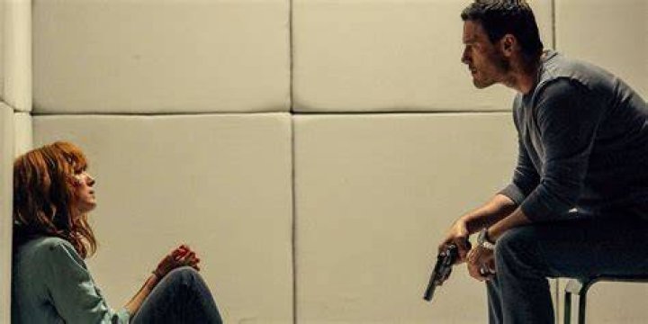 Kelly Reilly looking sideways while sitting on the floor while Luke Ewans sits on a chair with a gun in his hand in 10x10